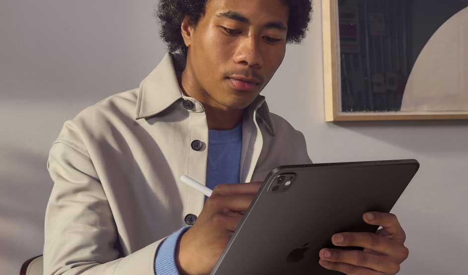 Een persoon schrijft of tekent met een Apple Pencil op een donkere Apple iPad in een lichte kamer met kunst aan de muur op de achtergrond.