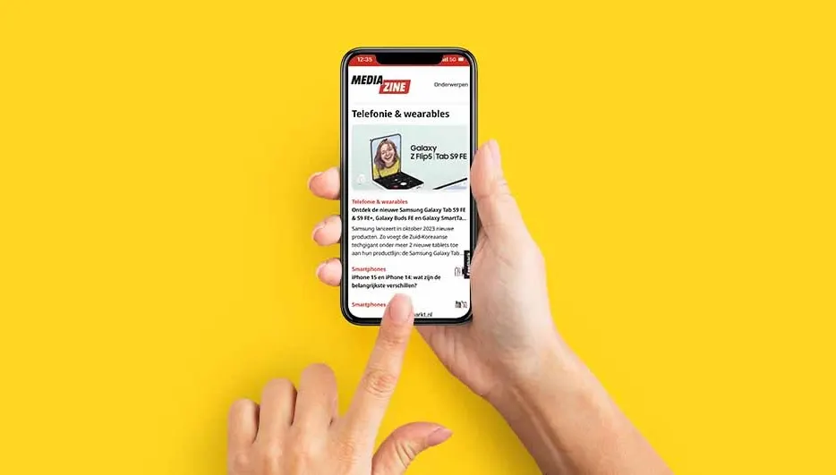 Handen houden een telefoon met een artikel over technologie tegen een gele achtergrond. De vinger wijst naar het scherm.