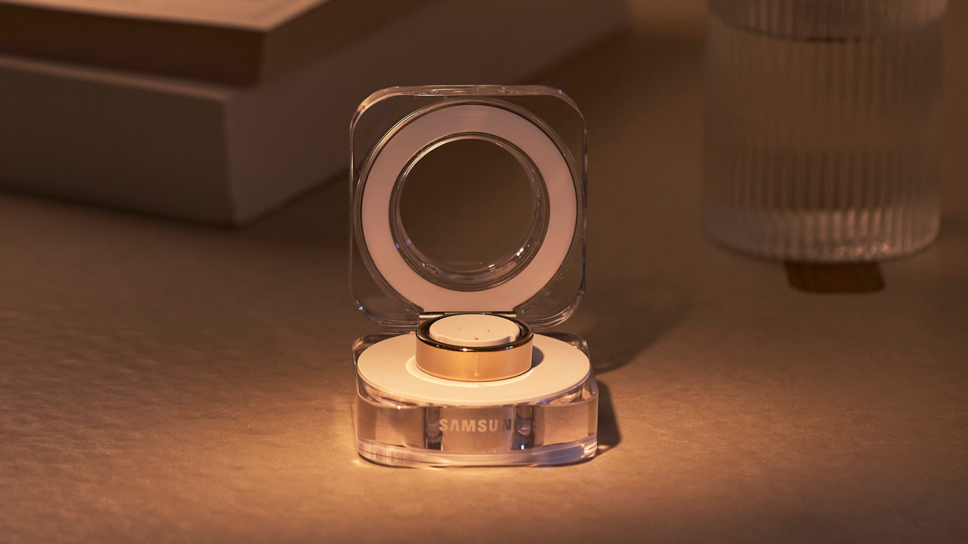 Een doorzichtige draadloze oplader met Samsung-logo, open met een gouden horloge-accessoire erop, op een tafel.