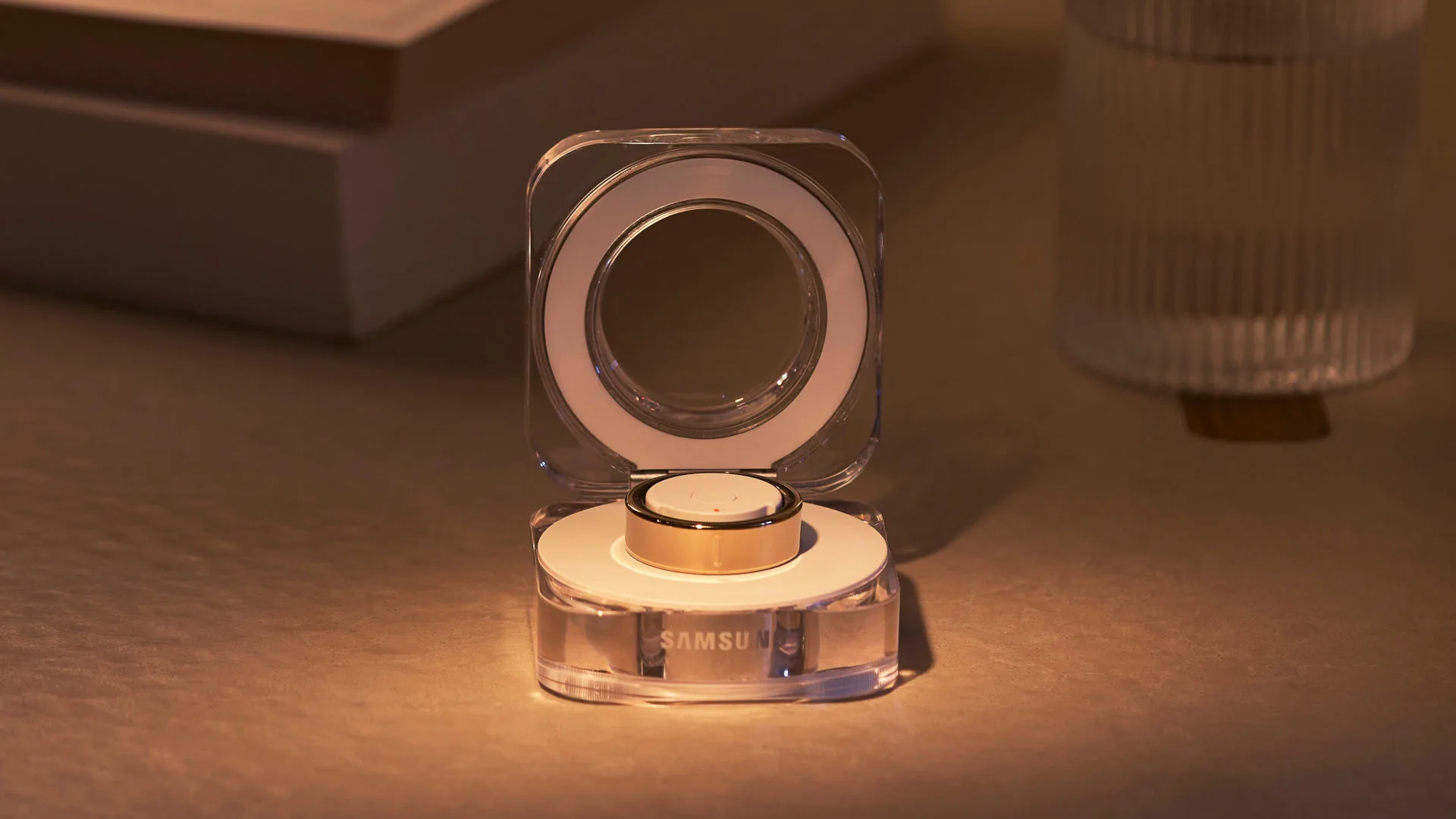 Een doorzichtige draadloze oplader met Samsung-logo, open met een gouden horloge-accessoire erop, op een tafel.