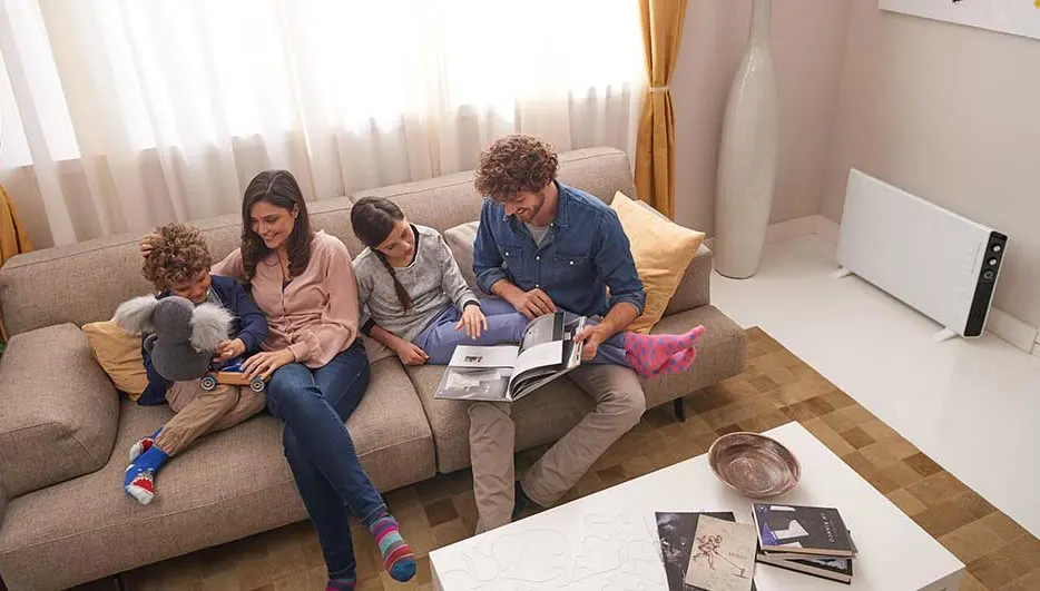 Een gezin van vier geniet op de bank met boeken en plezier. De kamer is warm dankzij een elektrische verwarming op de achtergrond.