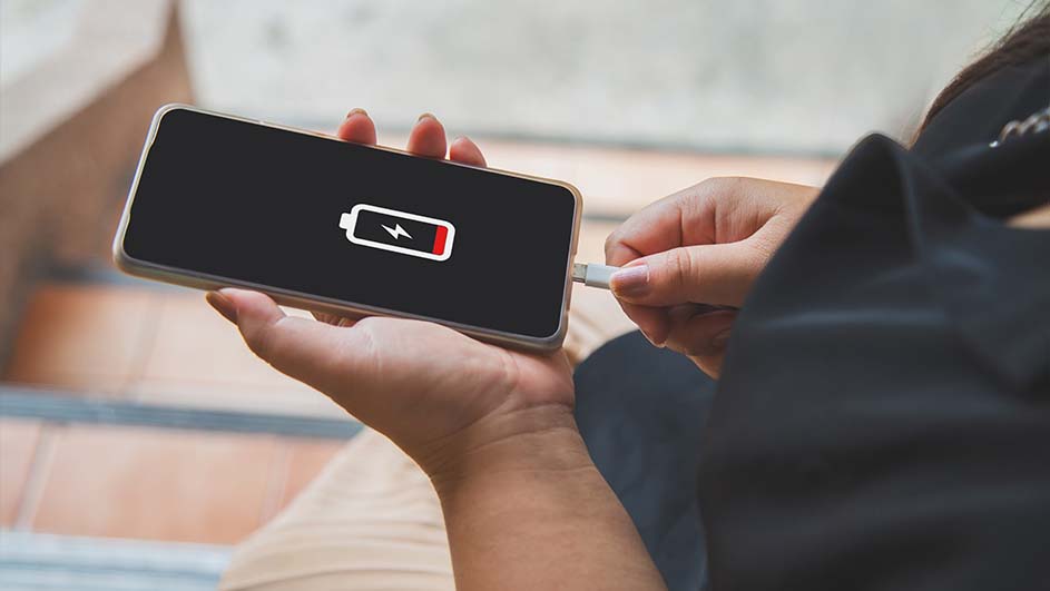 Een persoon houdt een zwarte smartphone vast met een rood batterijpictogram en een witte kabel wordt aangesloten.
