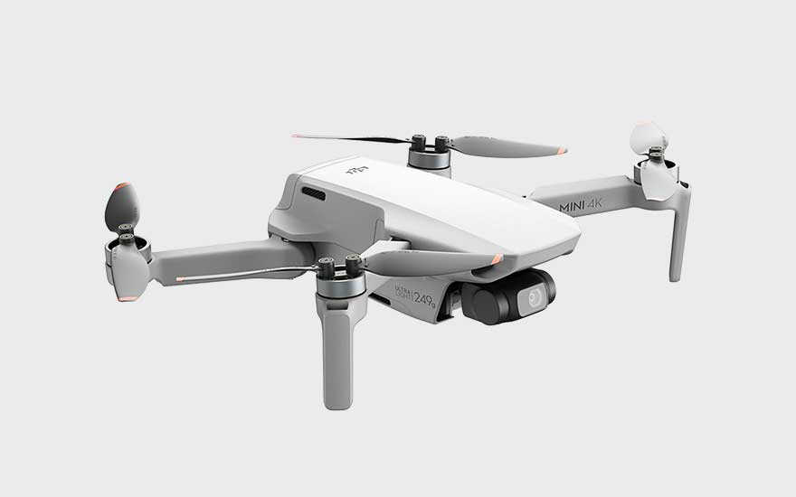 Een lichte drone staat afgebeeld op een witte achtergrond, met opzichtige propellers en een camera aan de voorkant. 