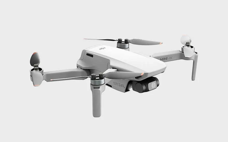 Een lichte drone staat afgebeeld op een witte achtergrond, met opzichtige propellers en een camera aan de voorkant.