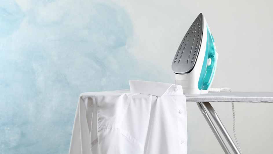 Een strijkijzer staat op een strijkplank naast een wit overhemd, tegen een blauw-witte achtergrond.