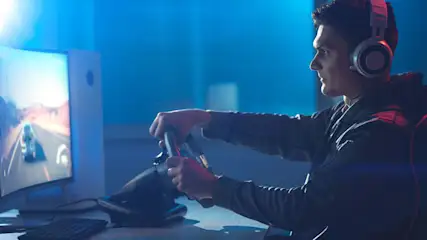 Een persoon met een koptelefoon speelt een racegame met een stuurwiel voor een computerscherm.