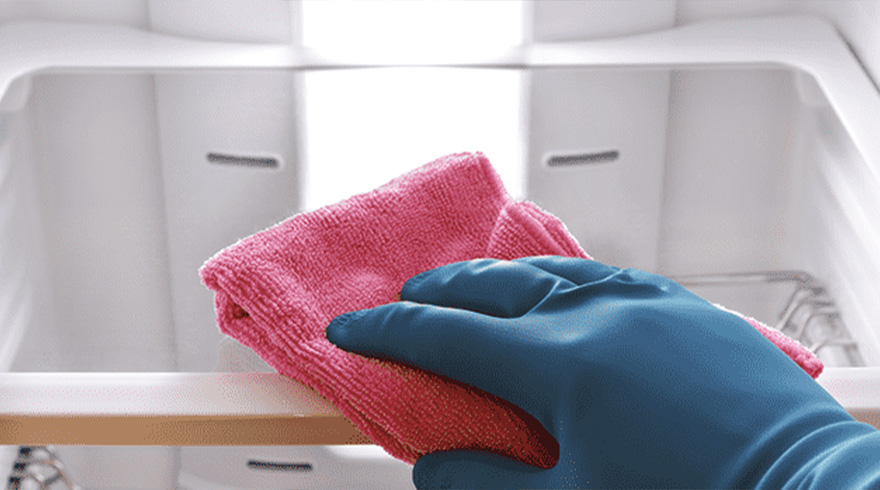 Een blauwe gehandschoende hand houdt een roze doek vast tegen een witte kast.