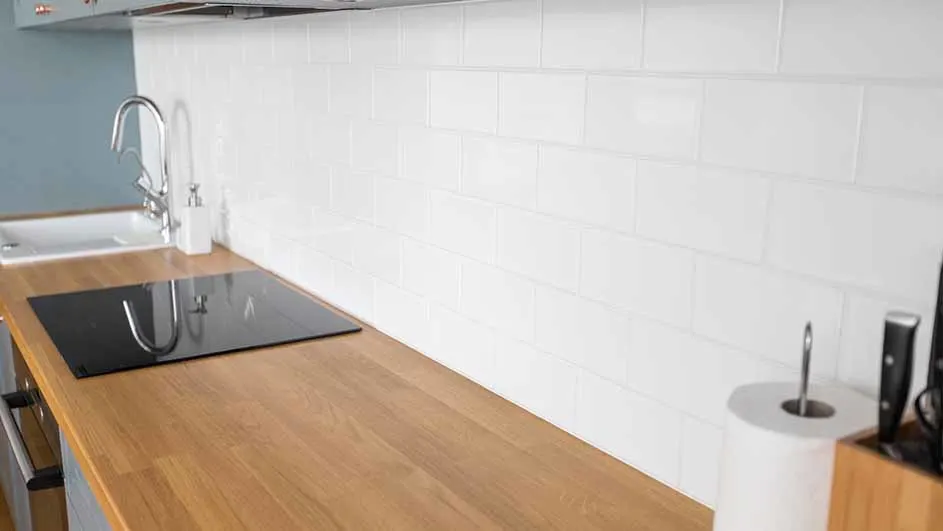 Een keuken met een houten aanrechtblad, een zwarte kookplaat en een gootsteen met een zilveren kraan tegen een witte achtergrond.