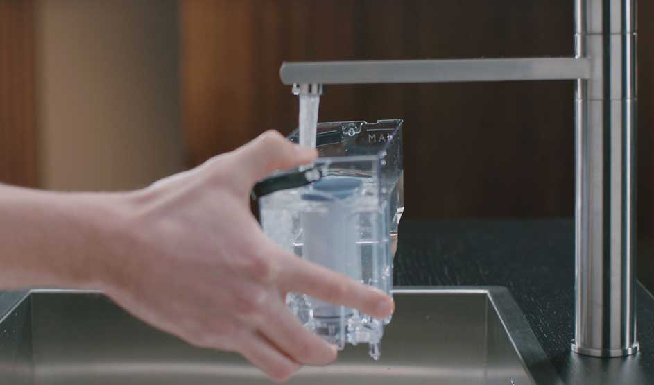 Een hand vult een Philips-waterreservoir onder een stromende keukenkraan, met een ingebouwd filter zichtbaar in het doorzichtige bakje.