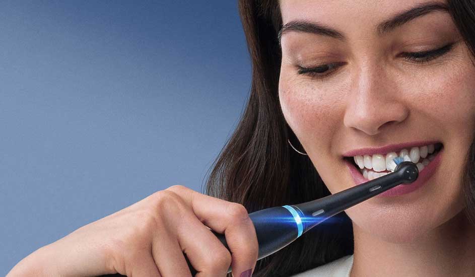 Een hand houdt een donkerblauwe elektrische trimmer van het merk Philips tegen lang bruin haar, met een egale blauwe achtergrond.