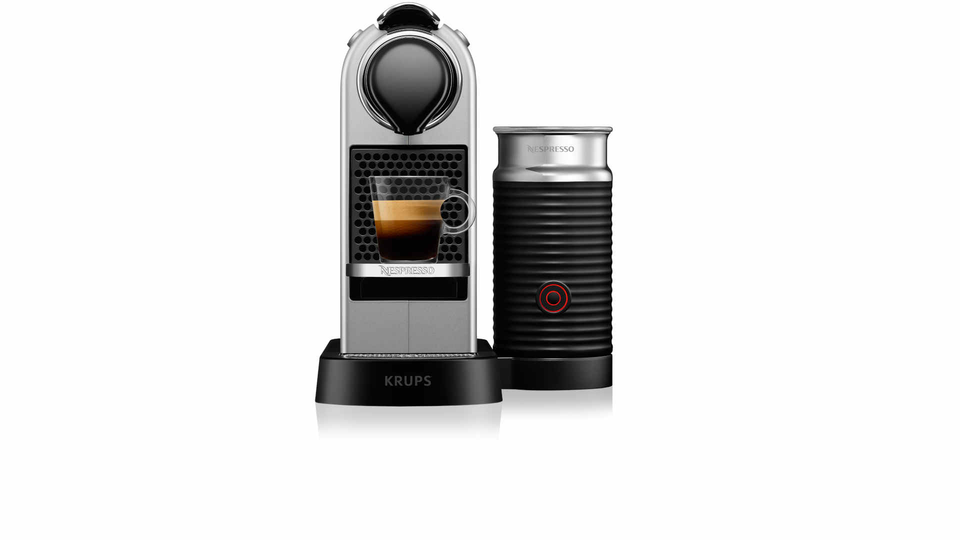 Een zilverkleurige Nespresso-machine met een kopje koffie ernaast en een zwarte melkopschuimer op een witte achtergrond.
