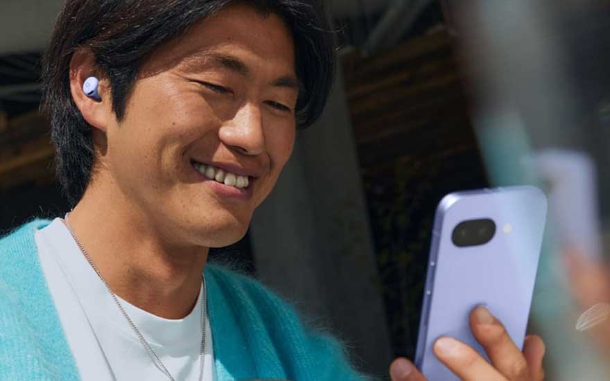 Een man glimlacht terwijl hij naar zijn smartphone kijkt, met Pixel Buds in zijn oren, genietend van muziek of een gesprek.