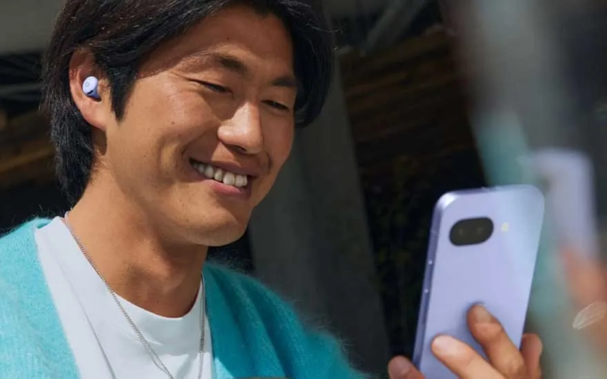 Een man glimlacht terwijl hij naar zijn smartphone kijkt, met Pixel Buds in zijn oren, genietend van muziek of een gesprek.