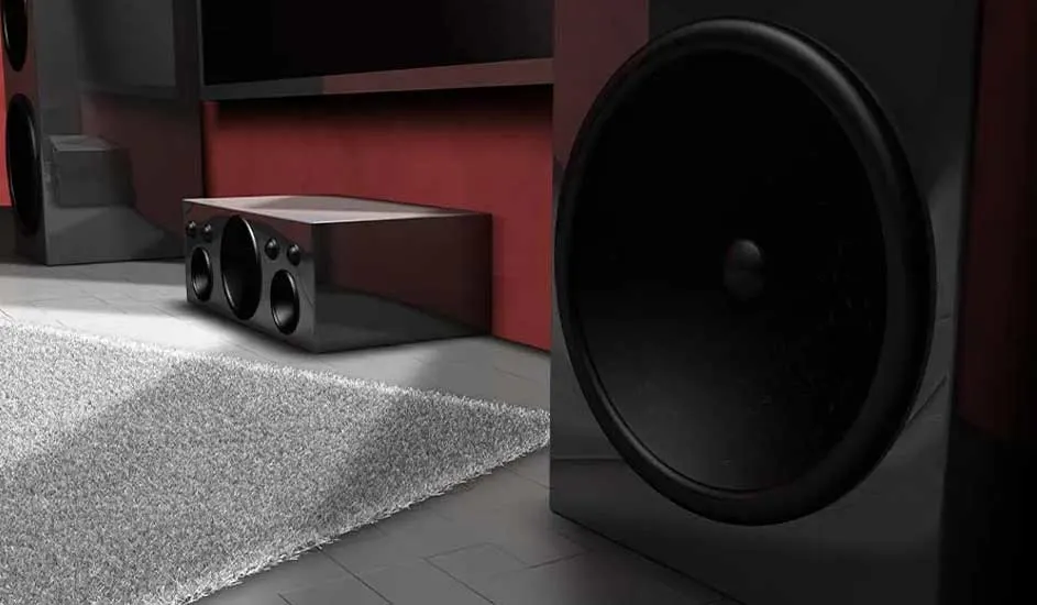 Home cinema with black speakers, subwoofer, and a red wall. Soft grey carpet on the floor for comfort and immersive sound.
