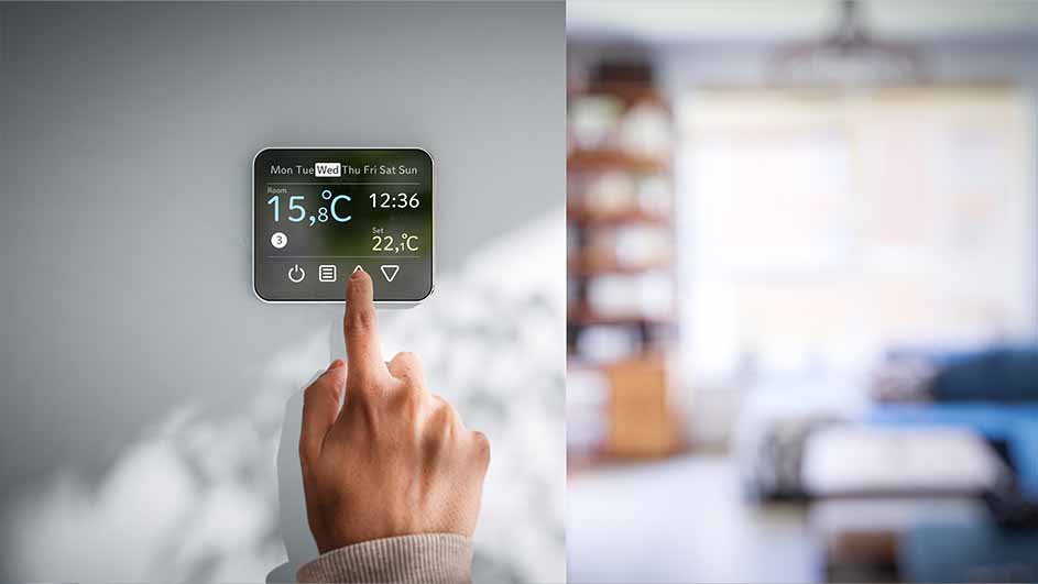 Een hand bedient een digitale thermostaat aan een muur, met een onscherpe woonkamer op de achtergrond. De display toont 15,8°C en 12:36.
