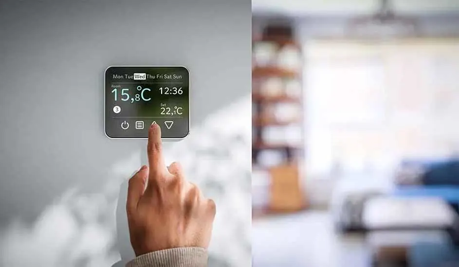 A hand adjusts a digital thermostat displaying 15.8°C, set to 22.1°C, with blurred living room background.
