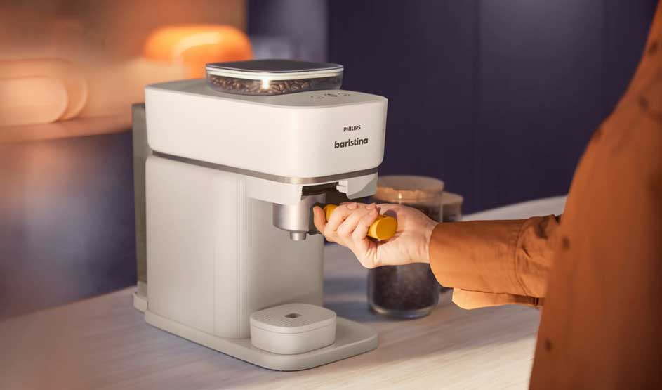 Een persoon plaatst een portafilter in een witte koffiemachine, met een glas koffie ernaast en warme verlichting op het aanrecht.