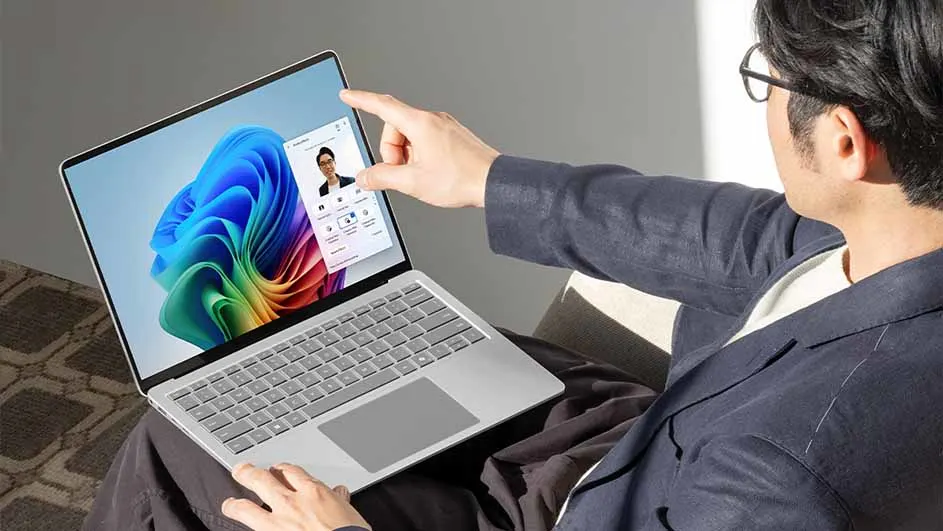 Man gebruikt een laptop met een kleurrijk scherm en een video-oproepvenster. Hij draagt een blauw jasje en een bril.