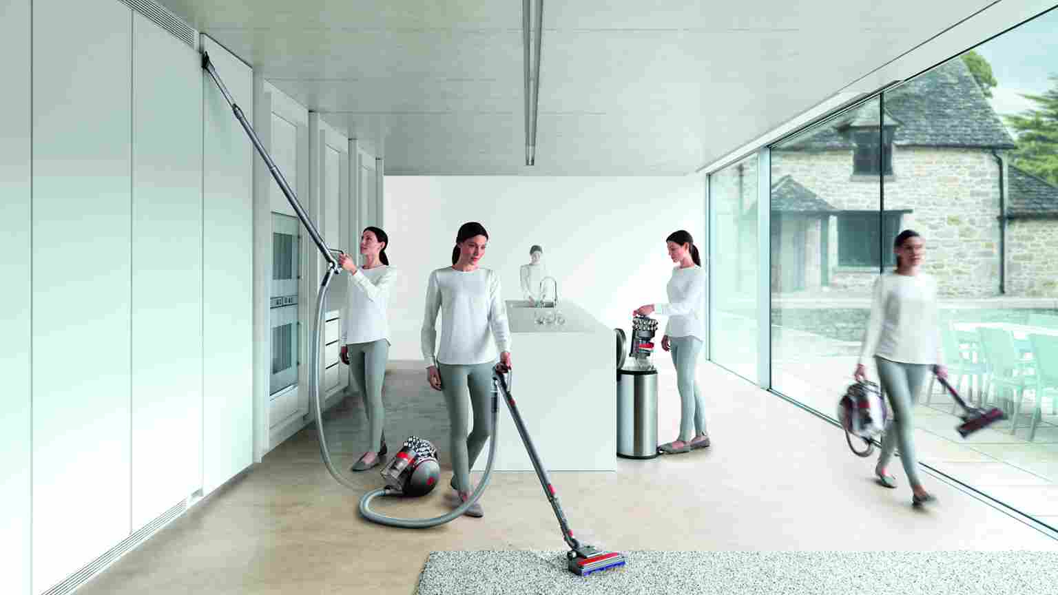 Een vrouw gebruikt een stofzuiger in een moderne ruimte met witte muren en grote ramen die uitkijken op een stenen gebouw en een zwembad.
