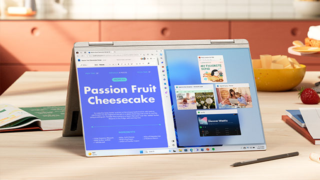 Een 2-in-1 laptop staat op een tafel met een recept voor passievruchtencheesecake op het scherm. Een gele kom met fruit staat ernaast.