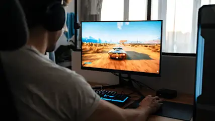 Een persoon met een koptelefoon speelt een racegame op een monitor. Het toont een auto op een zanderige weg.