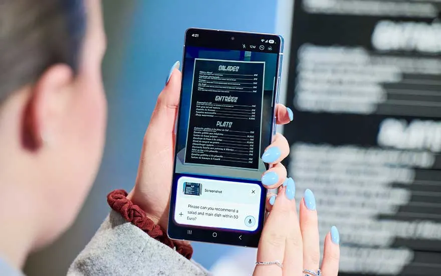 Een vrouw houdt een Samsung-smartphone verticaal en scant een restaurantmenu, terwijl AI-tekst onderaan suggesties of vertaling toont.