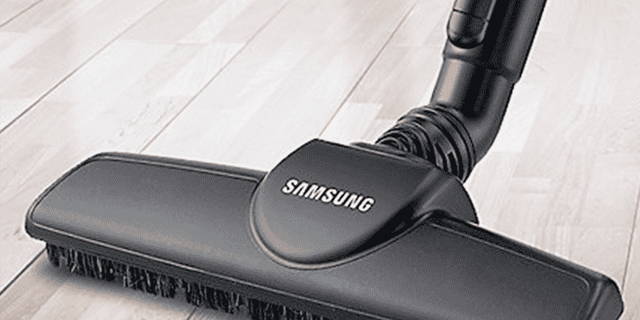 Een zwarte Samsung stofzuigerkop met borstels staat op een lichtgekleurde houten vloer. De slang is aan de stofzuigerkop bevestigd.