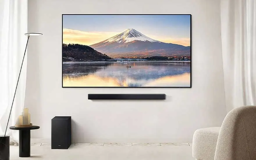 Strakke witte woonkamer met grote tv waarop Mount Fuji te zien is, soundbar, subwoofer, stoel en moderne vloerlamp.