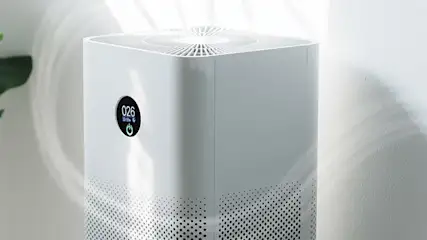 Een witte luchtreiniger met een digitaal display dat "026" toont, staat tegen een lichte achtergrond.