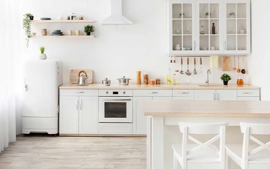 Een lichte, moderne keuken met witte kasten, houten werkblad en open planken. Kookgerei hangt aan een rail en vitrinekast toont servies. Minimalistisch en gezellig.