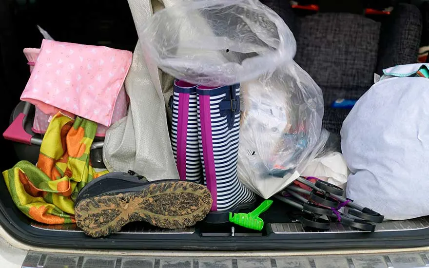 The boot of a car is filled with muddy boots, a plastic bag, blankets and hiking poles, everything jumbled together in a mess.