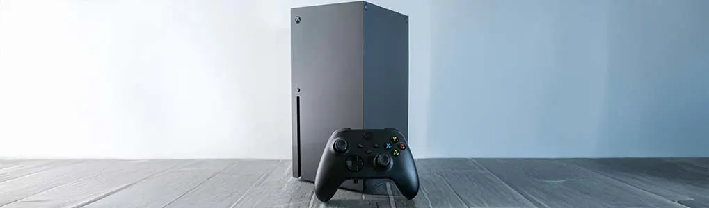 Een zwarte Xbox-console met bijpassende controller, minimalistisch gepositioneerd op een houten vloer tegen een lichte achtergrond.