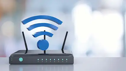 Zwarte router met blauw wifi-symbool en indicatielampjes op een lichte tafel tegen een vage achtergrond.