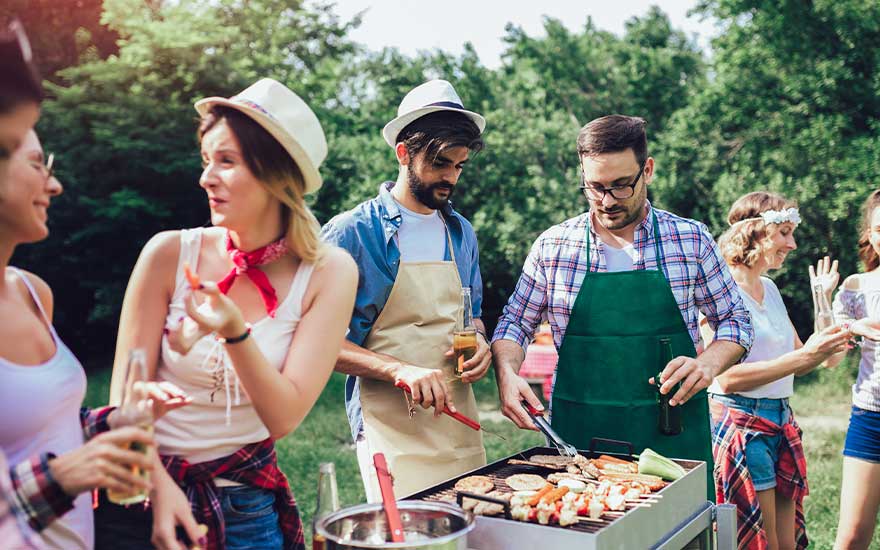 Vrienden genieten van een zomerse barbecue in het park, terwijl twee mannen schorten dragen en vlees en groenten grillen.