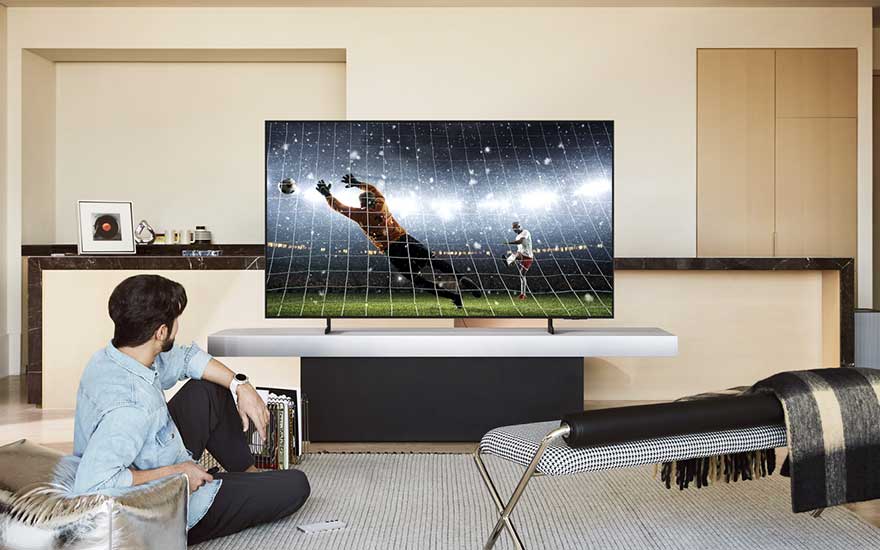 Een man zit in een minimalistische woonkamer en kijkt naar een tv waarop een keeper een spectaculaire redding maakt.
