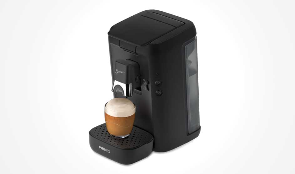 Een zwarte koffiemachine staat op een lichte achtergrond en vult een klein glas met koffie, bekroond met een dikke schuimlaag.
