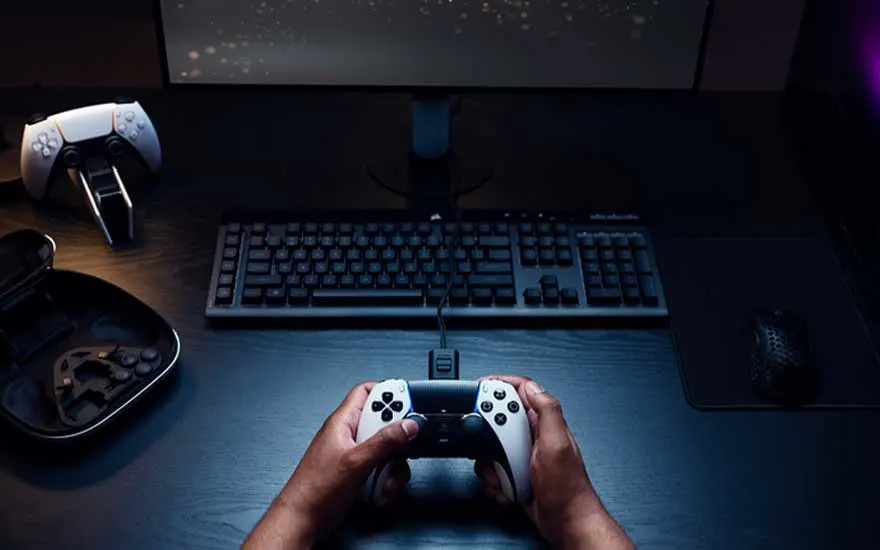 Bovenaanzicht van een gaming setup met toetsenbord en muis; iemand houdt een bekabelde DualSense controller vast, helemaal klaar om te spelen.