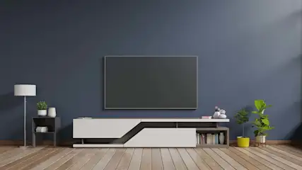 Een woonkamer met een tv aan een blauwe muur, een witte tv-meubel, een lamp en planten op een houten vloer.
