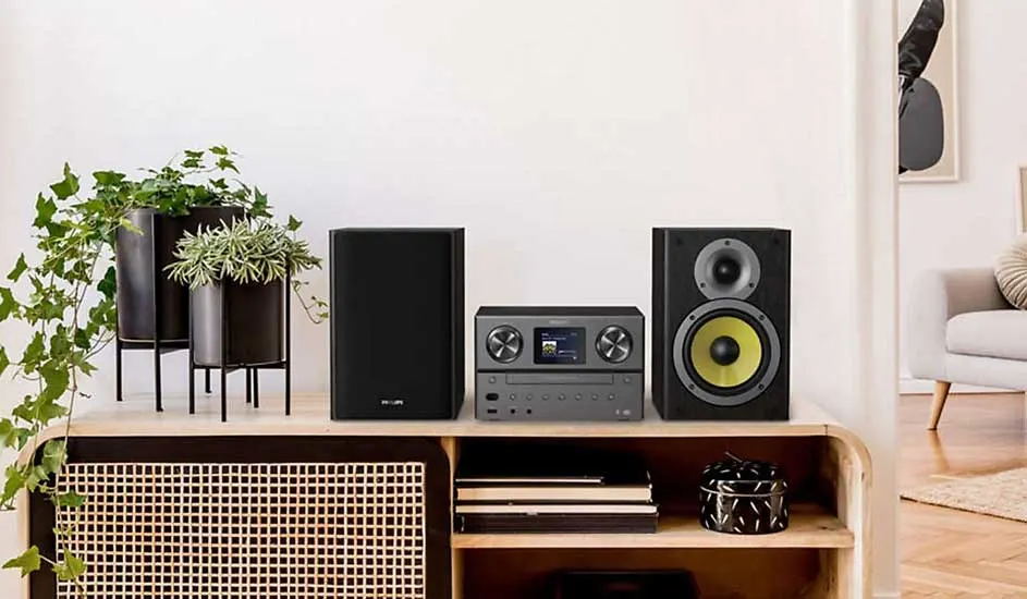 Op een houten kast staan twee planten, een Philips stereo-installatie met speakers, en decoratie in een lichte, moderne woonkamer.