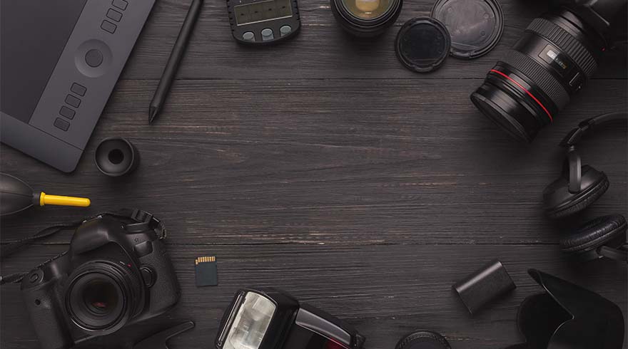 Een donkere houten tafel met een tekentablet, camera, lenzen, hoofdtelefoon en geheugenkaart.