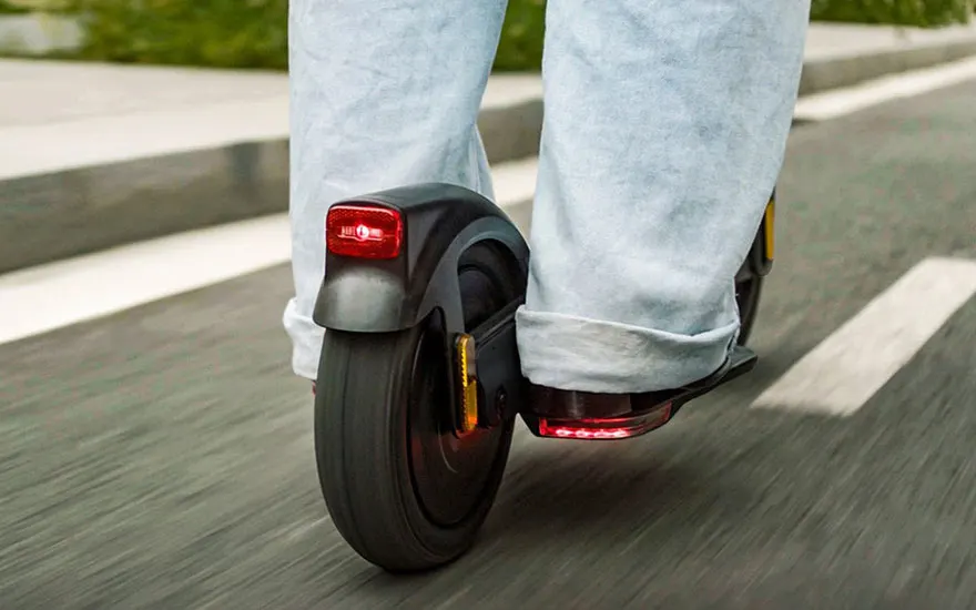 Dynamische opname van iemand in spijkerbroek die op een zwarte step rijdt, met rode achterlichten en bewegingseffect op de weg.