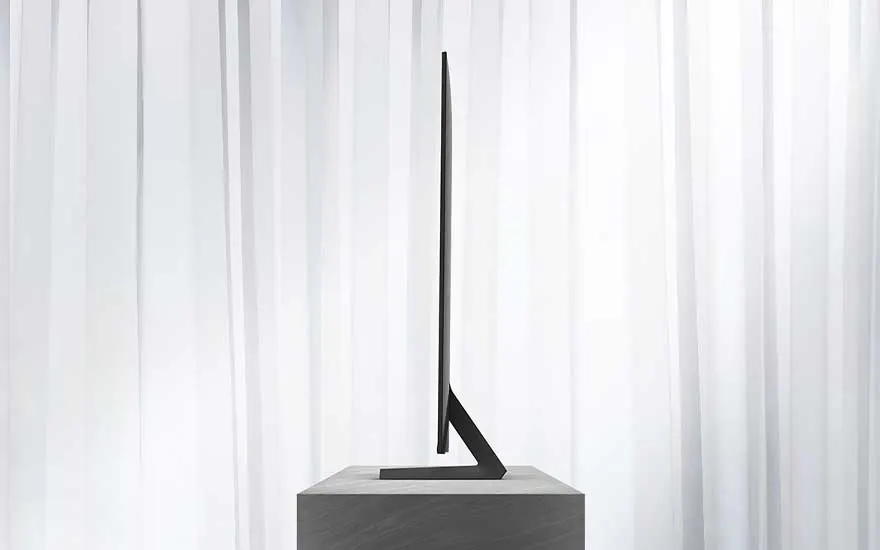 Zijaanzicht van een ultradunne televisie die op een moderne standaard staat, met op de achtergrond lichte, doorschijnende gordijnen.