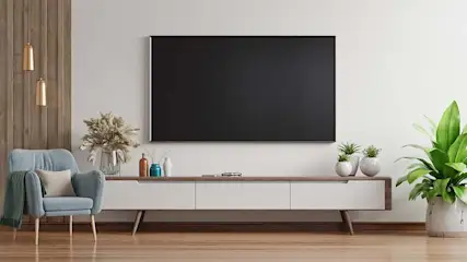 Een woonkamer met een grote tv aan de muur, een blauwe stoel en planten op een wit tv-meubel.