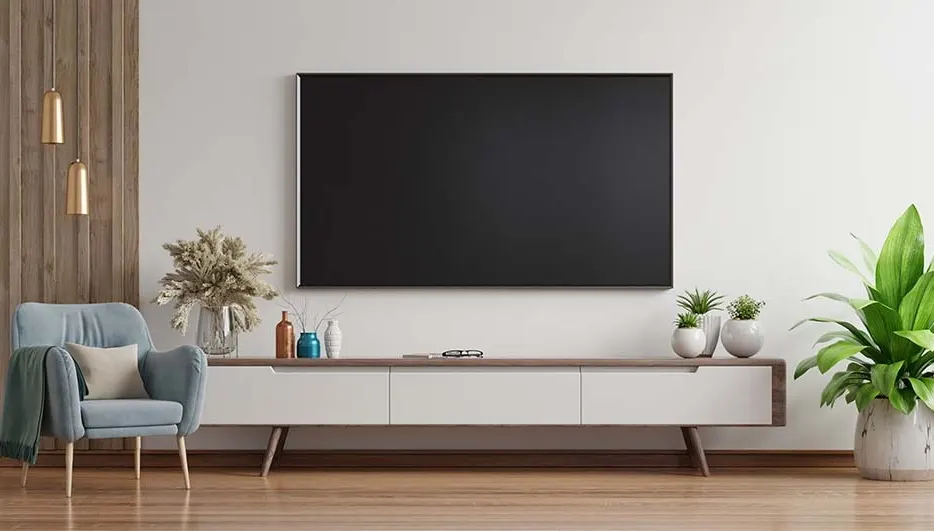Een woonkamer met een grote tv aan de muur, een blauwe stoel en planten op een wit tv-meubel.