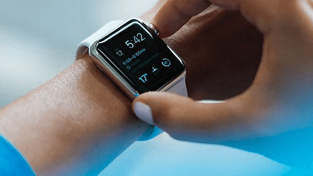 Pols met een zilverkleurige smartwatch met een wit bandje, waarop de tijd 12:5:42 staat. Een vinger raakt het scherm aan.