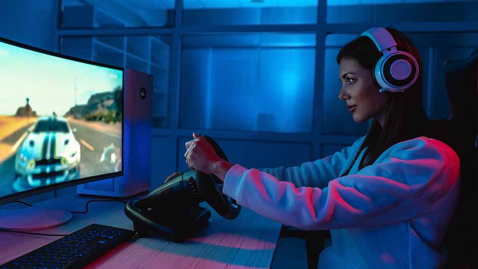 Vrouw met koptelefoon speelt een racegame met stuurwiel voor een monitor. Een toetsenbord staat op de tafel.