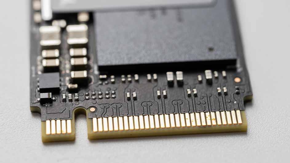 Close-up van een zwarte solid-state drive met goudkleurige contactpunten en diverse elektronische componenten.