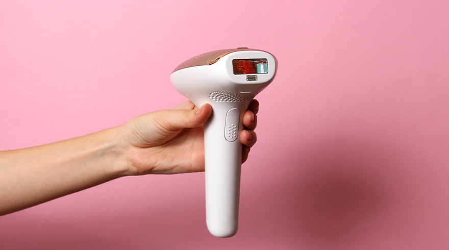 Hand houdt een wit en gouden laserapparaat tegen een roze achtergrond.