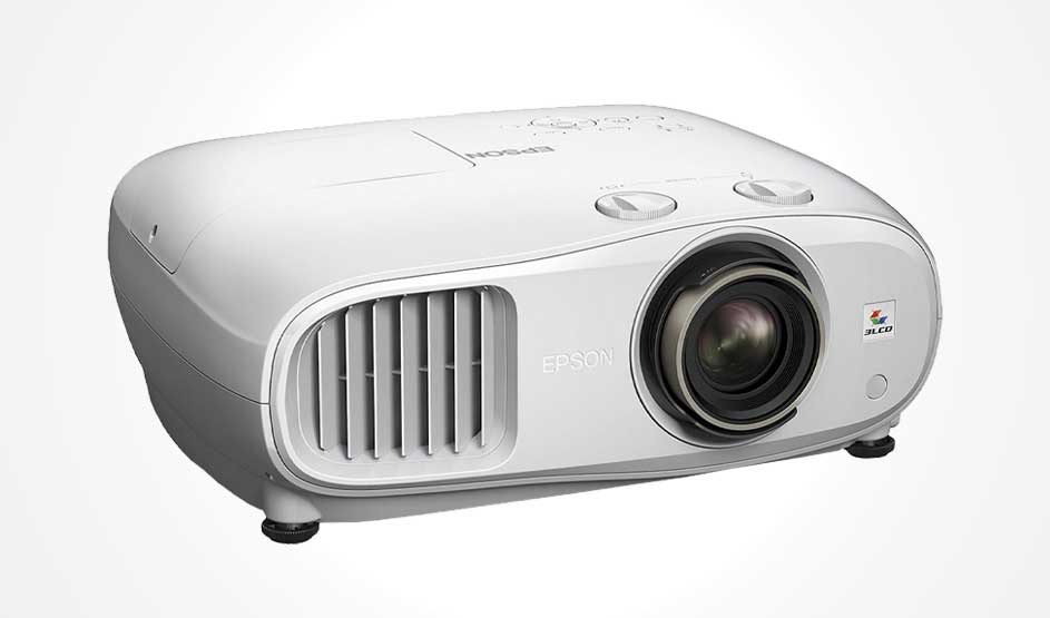 Een witte Epson-projector met grote lens en ventilatierooster staat schuin op een lichte achtergrond.