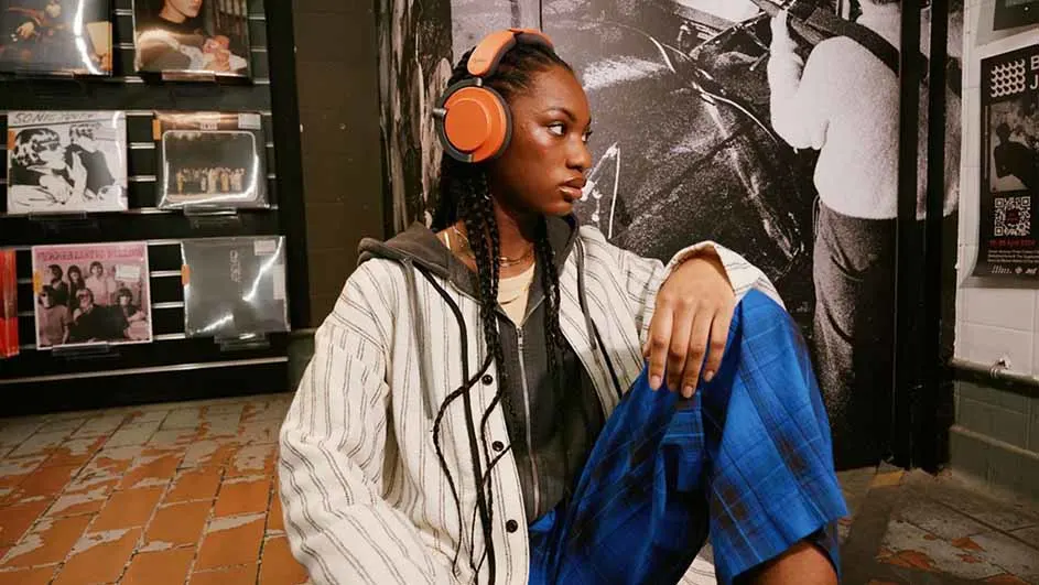 Een persoon met een oranje koptelefoon zit voor een wand met vinylplaten en een zwart-wit foto.